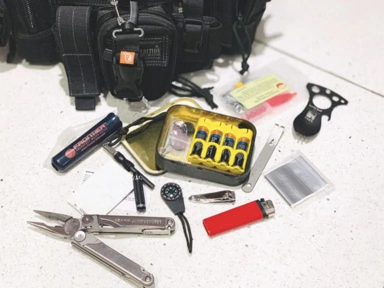 survival kit items displayed on the floor next to an altoids tin