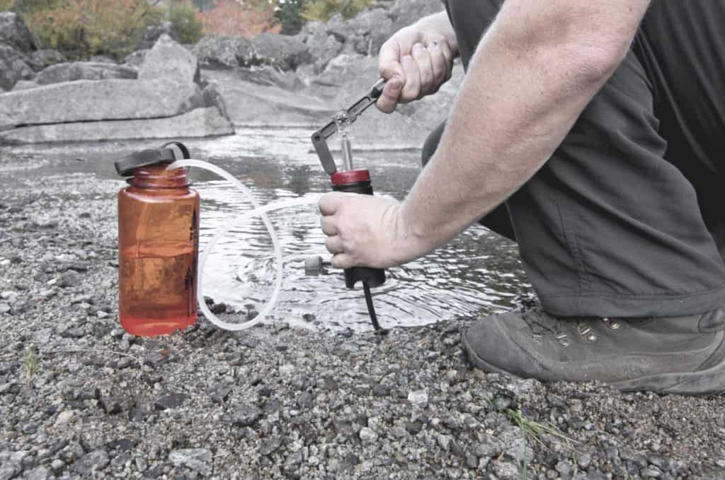 man filling water bottle with filtered water from the river