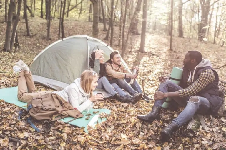 4 adult friends sitting by their tent in the woods laughing