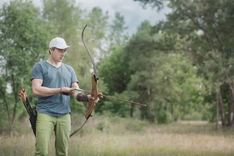 man holding an archery bow getting ready to shoot an arrow in the forest
