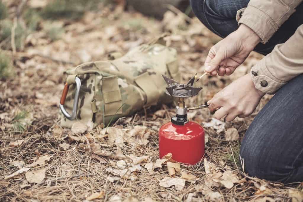 person in wilderness ignites camping stove to boil water