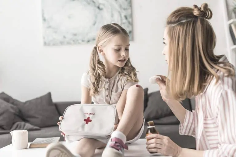 mother treating little girls cut on her knee while holding home first aid kit