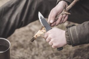 close up of hunter using a fixed blade knife to cut a stick in the wild
