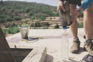 man filling water bottle from a gravity water filter while hiking outdoors