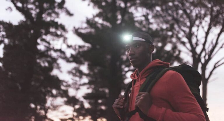 man standing in woods with backpack and headlamp on head