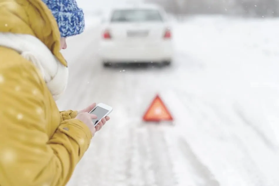 young woman calling emergency services after car break down in the snow
