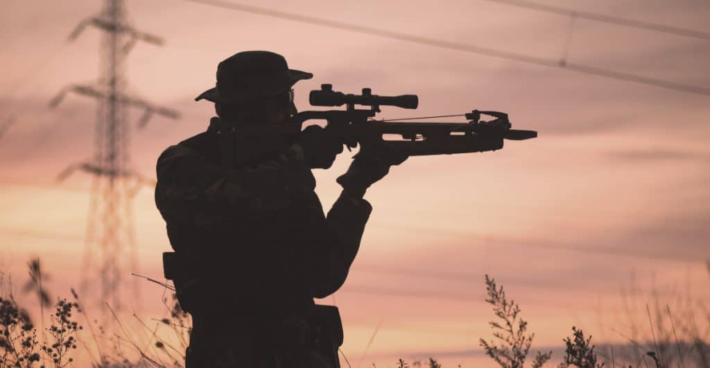 silhouette of a man holding a crossbow during a sun set