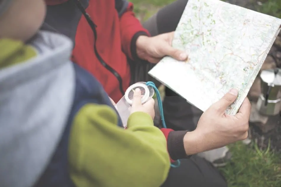 dad holding map and boy holding compass in woods