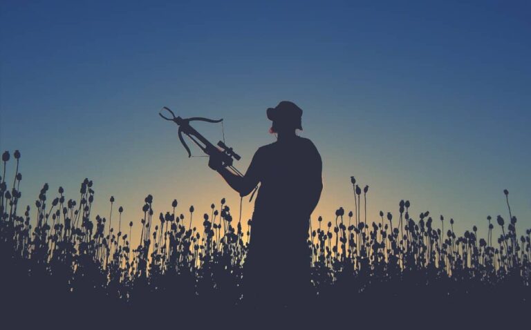 man standing in field holding a crossbow