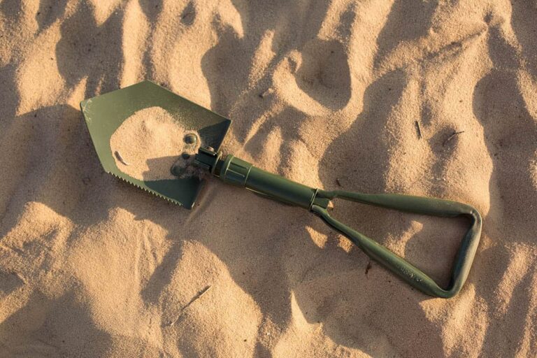 green folding shovel laying on ground in desert sand
