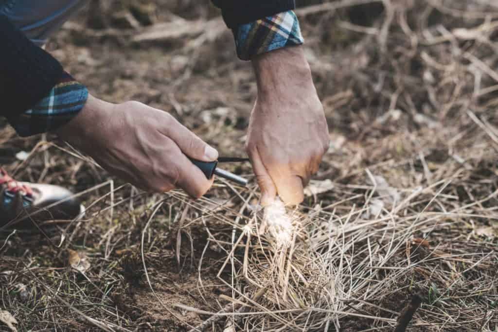 man holding a magnesium fire starter to start a fire for survival in the wild