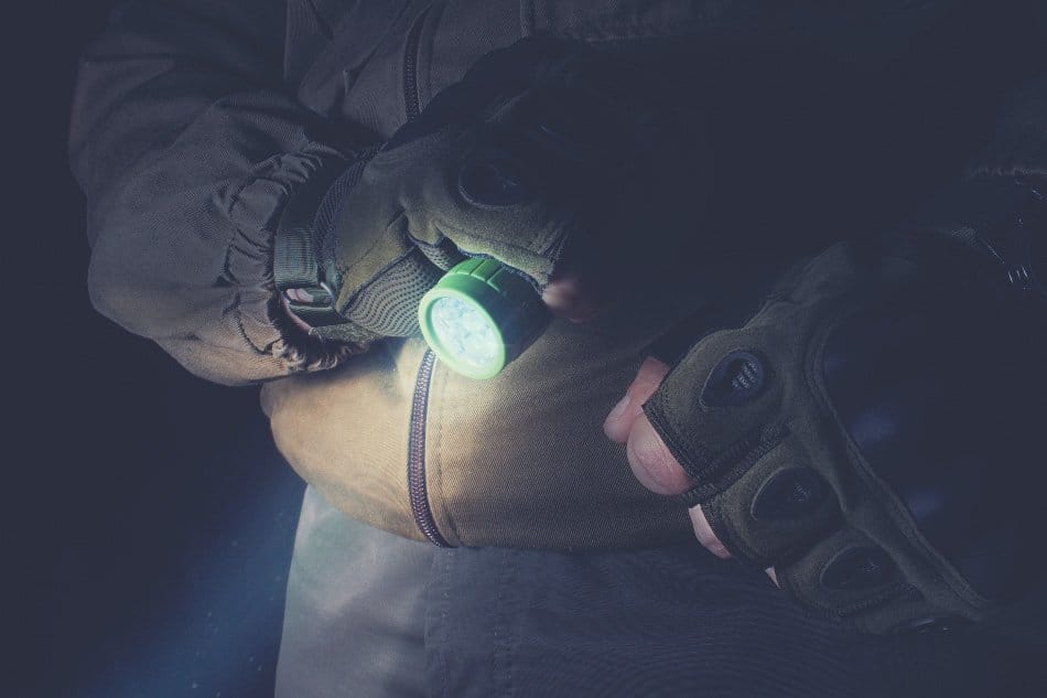 man holding flashlight in the dark wearing a tactical vest