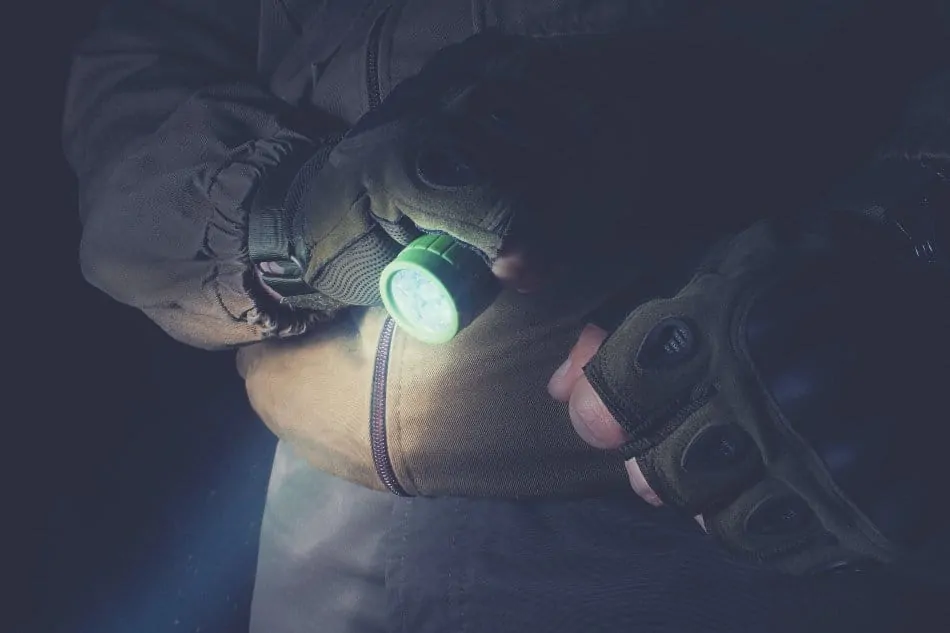 man holding flashlight in the dark wearing a tactical vest