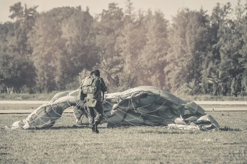 paratrooper landed in field gathering his parachute