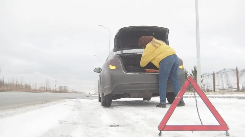 woman looking for goods in her trunk of broken down car in the snow