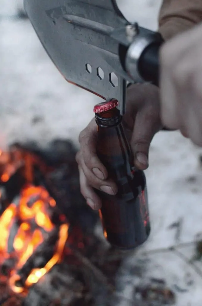survival shovel being used to open a beer bottle top