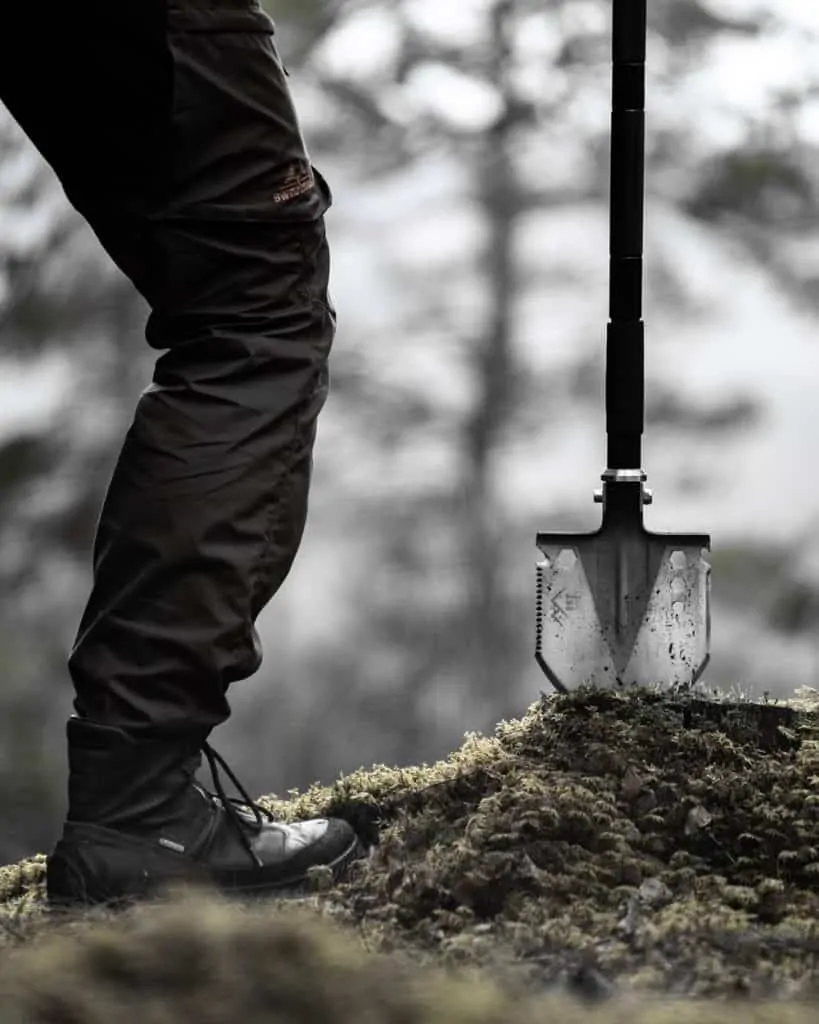 man holding survival shovel wedged into tree stump