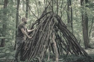 man building a survival shelter in the forest using tree branches and leaves