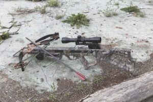 crossbow laid on ground in a safe position with arrows beside it