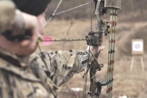 man taking aim at a target in the bush with a compound bow