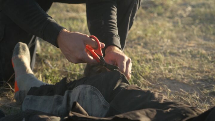 A Person Is Cutting Through Clothing with Trauma Shears to Treat an Injury During a Tactical Combat Casualty Care Scenario